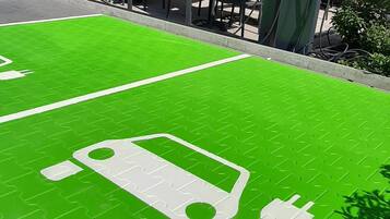 Una estación de carga para vehículos eléctricos al aire libre, con pavimento verde y un símbolo de coche eléctrico blanco.