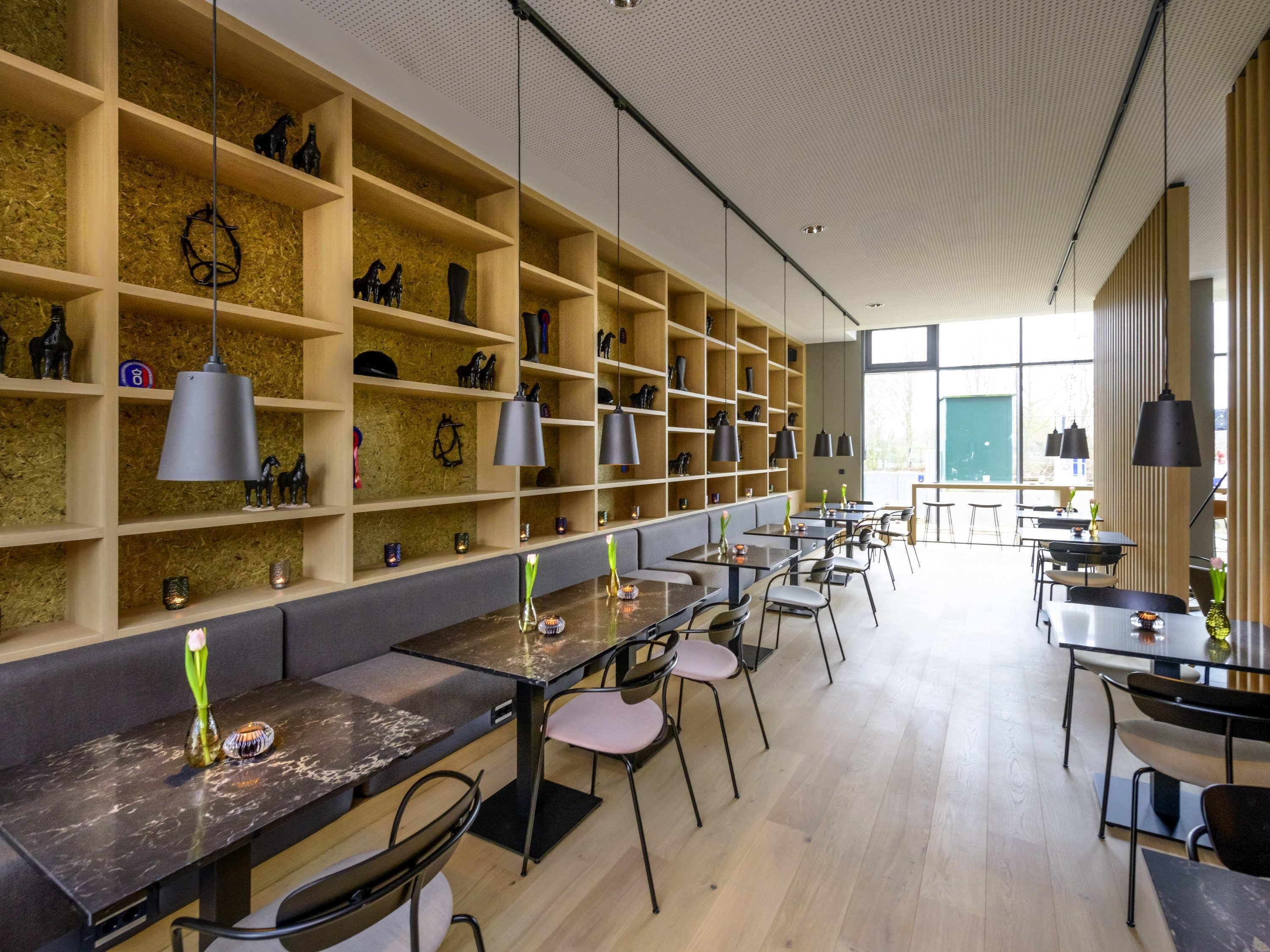 Een modern interieur met houten planken, tafels, stoelen, hanglampen en een groot raam dat natuurlijk licht binnenlaat.