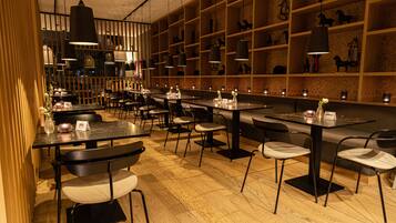 Un restaurante con varias mesas y sillas, pisos de madera e iluminación colgante.