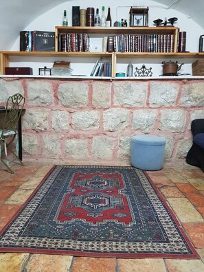 Une pièce avec un tapis à motifs, un mur en pierre et une bibliothèque remplie de livres et d’objets décoratifs.