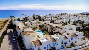 Una zona residencial costera con edificios blancos, una piscina central y vistas al mar.