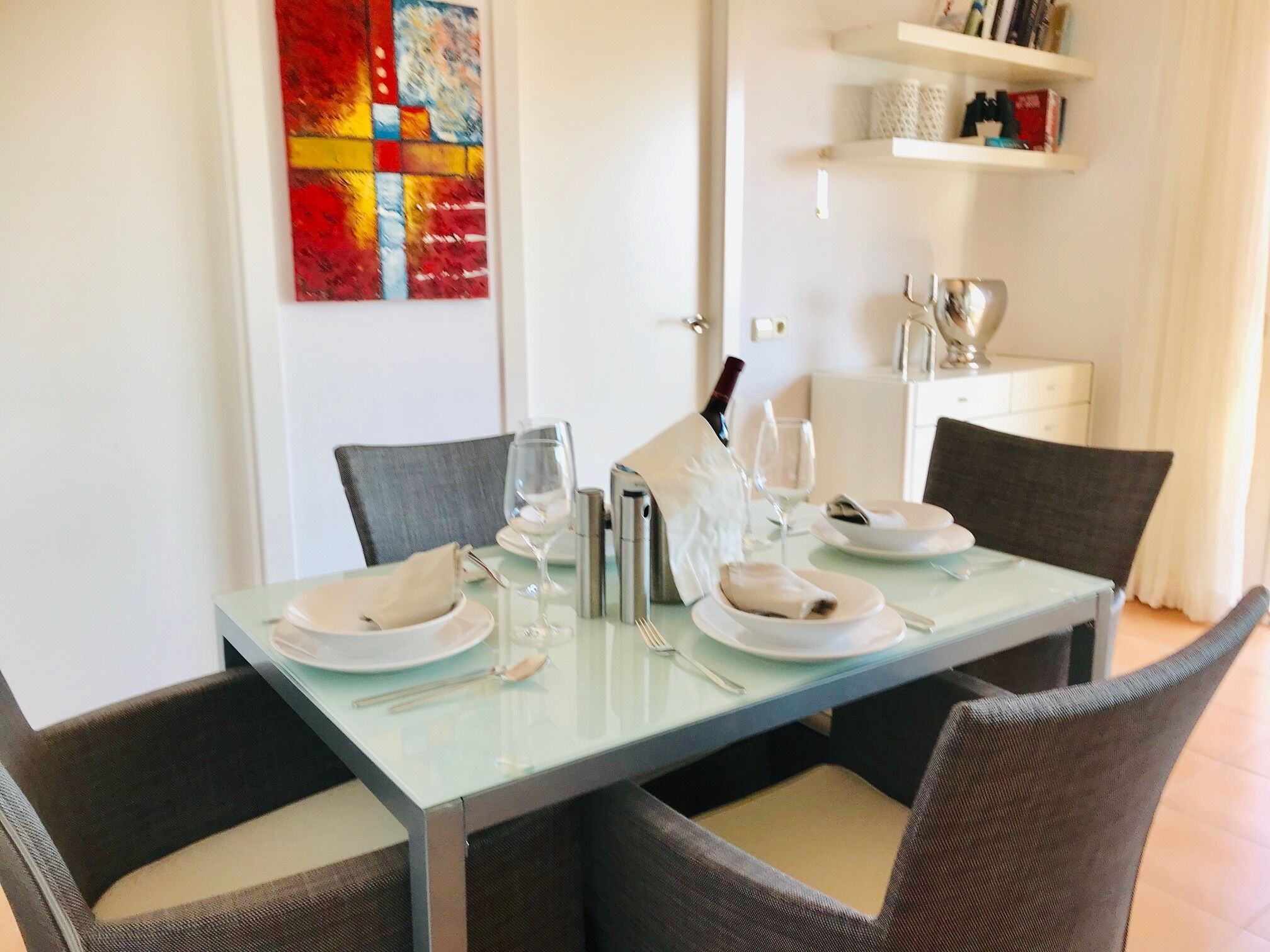 A dining table set for four with chairs, a wine bottle, and glasses.
