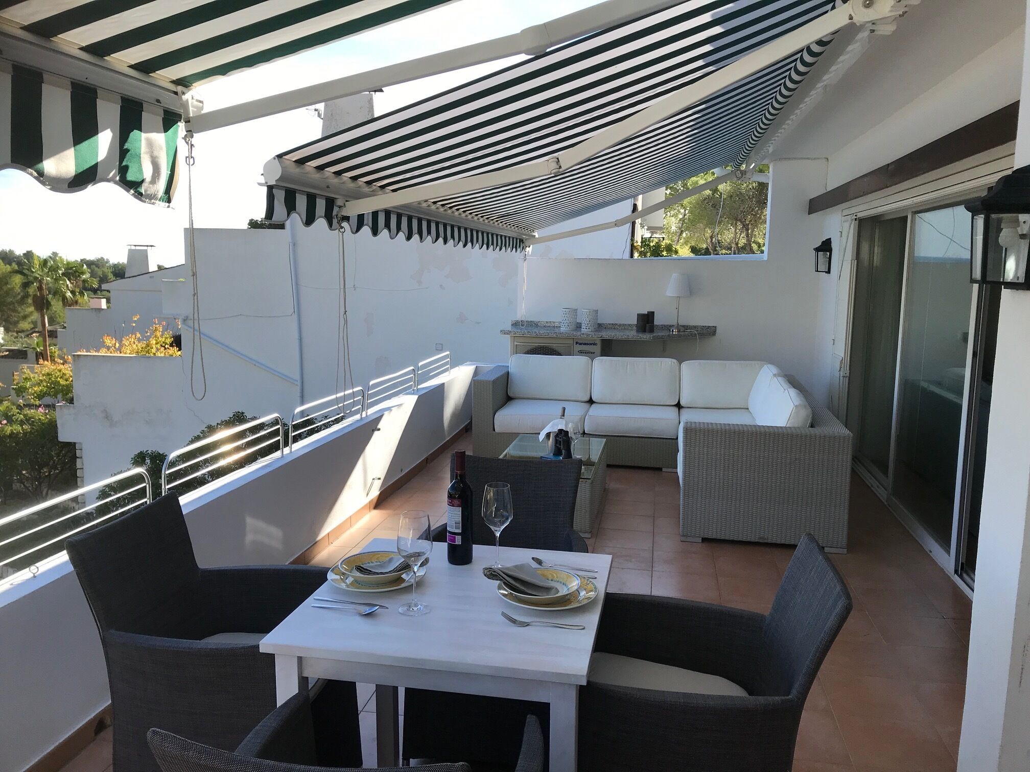 A rooftop terrace with a dining table set for two, outdoor seating, and a view of the surrounding area.