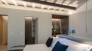 A modern bedroom with a large bed, a glass bedside table, a mirror, and a skylight. - Apartments Florence - Santo Spirito Exclusive (Firenze)