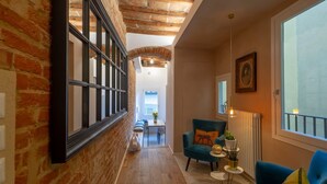 A hallway with exposed brick walls, a wooden floor, a blue armchair, a small table with a plant, and a radiator. - Apartments Florence - Santo Spirito Exclusive (Firenze)