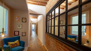 A hallway with a blue armchair, a brick wall, and framed pictures on the wall. - Apartments Florence - Santo Spirito Exclusive (Firenze)