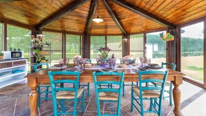 Un espace repas abrité, avec une table en bois dressée pour quatre personnes, entourée de chaises turquoise, et un sol recouvert de carreaux de pierre.