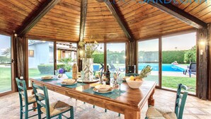 Un coin repas en bois, avec une table dressée pour quatre personnes, donnant sur une piscine et un espace verdoyant.