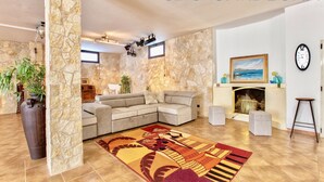 Un salon avec un mur en pierre, un canapé d’angle, une cheminée et un grand tapis.