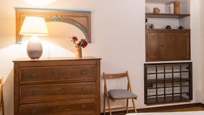 A wooden dresser with drawers, a lamp, a vase with flowers, a chair, and a shelf with kitchen items. - Piazza Navona Charming Apartment (Rome)