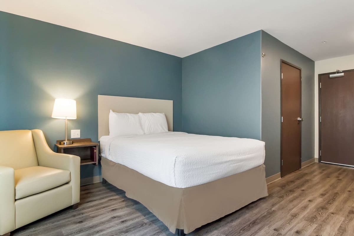 A hotel room with a bed, a chair, a nightstand, and a lamp.