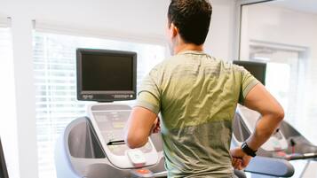 A person using a treadmill in a gym with a digital display and windows.