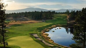 Un parcours de golf avec un étang, entouré d’arbres et avec des montagnes en arrière-plan.