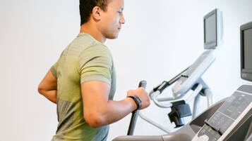 Eine Person trainiert auf einem Laufband in einem Fitnessstudio, das einen digitalen Bildschirm und eine Wandleinwand hat.
