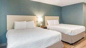 Une chambre d’hôtel avec deux lits, chacun doté d’une tête de lit et d’un oreiller blancs, d’une table de chevet avec une lampe, et de murs de couleur turquoise.