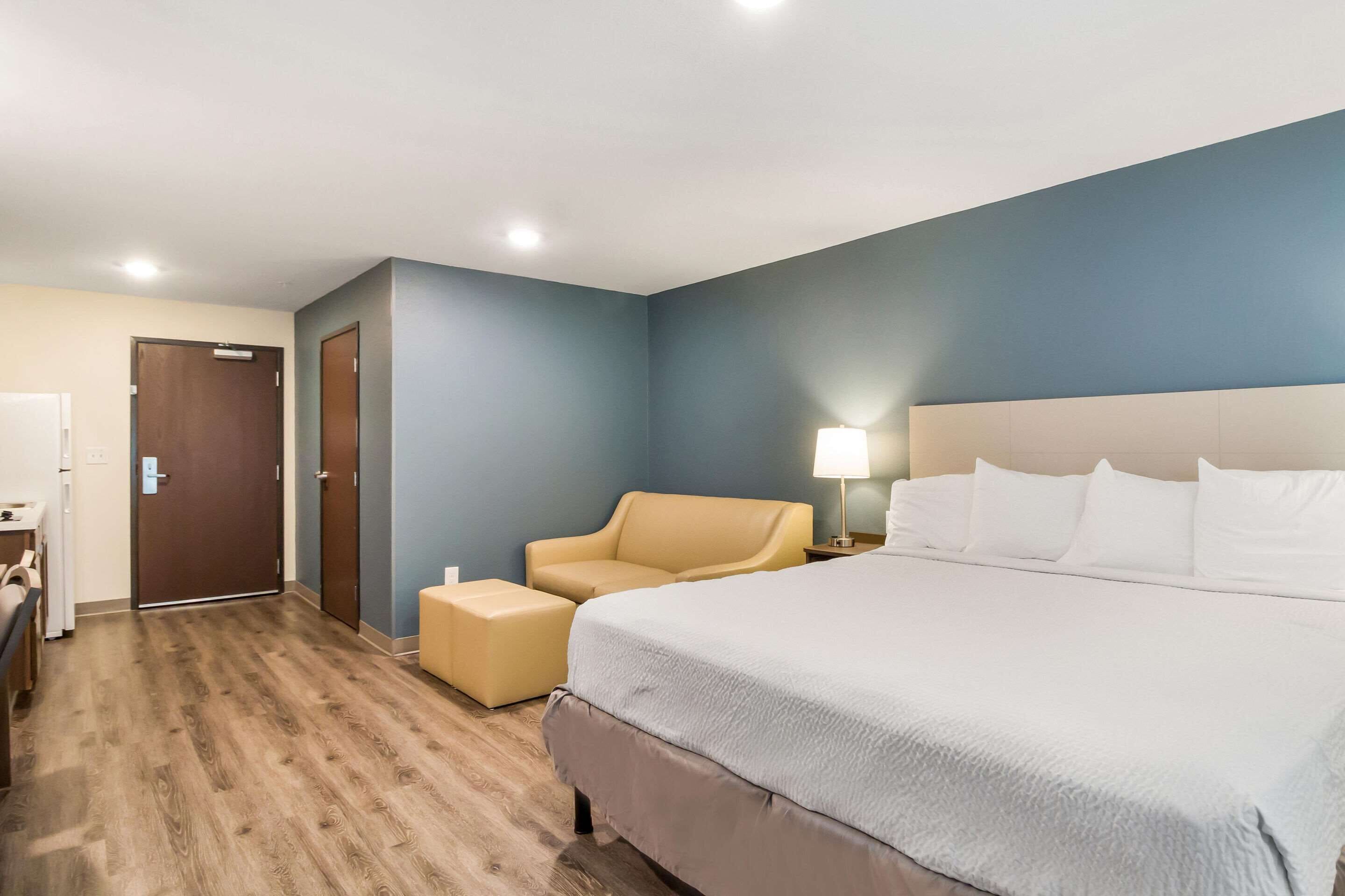 Una habitación de hotel con una cama grande, una silla, un escritorio y una puerta.