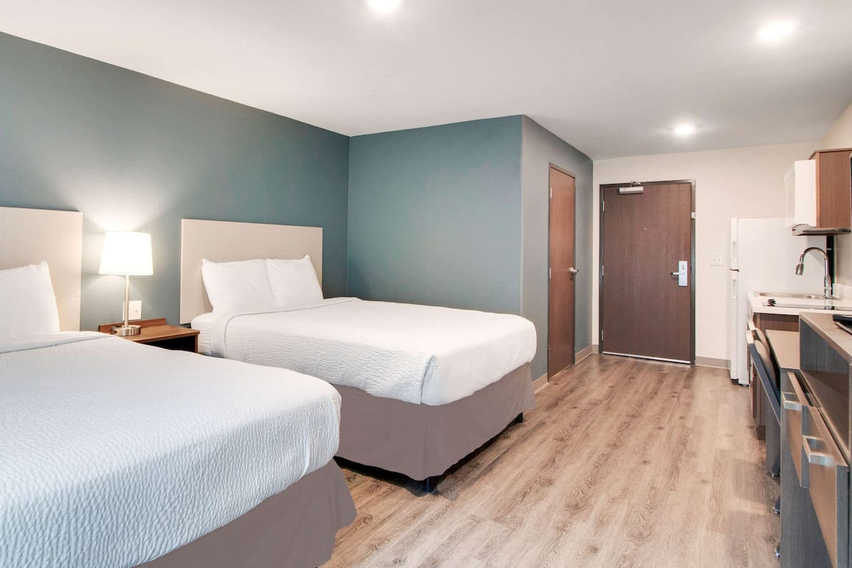 A hotel room with two beds, a desk, a chair, a lamp, and a door.