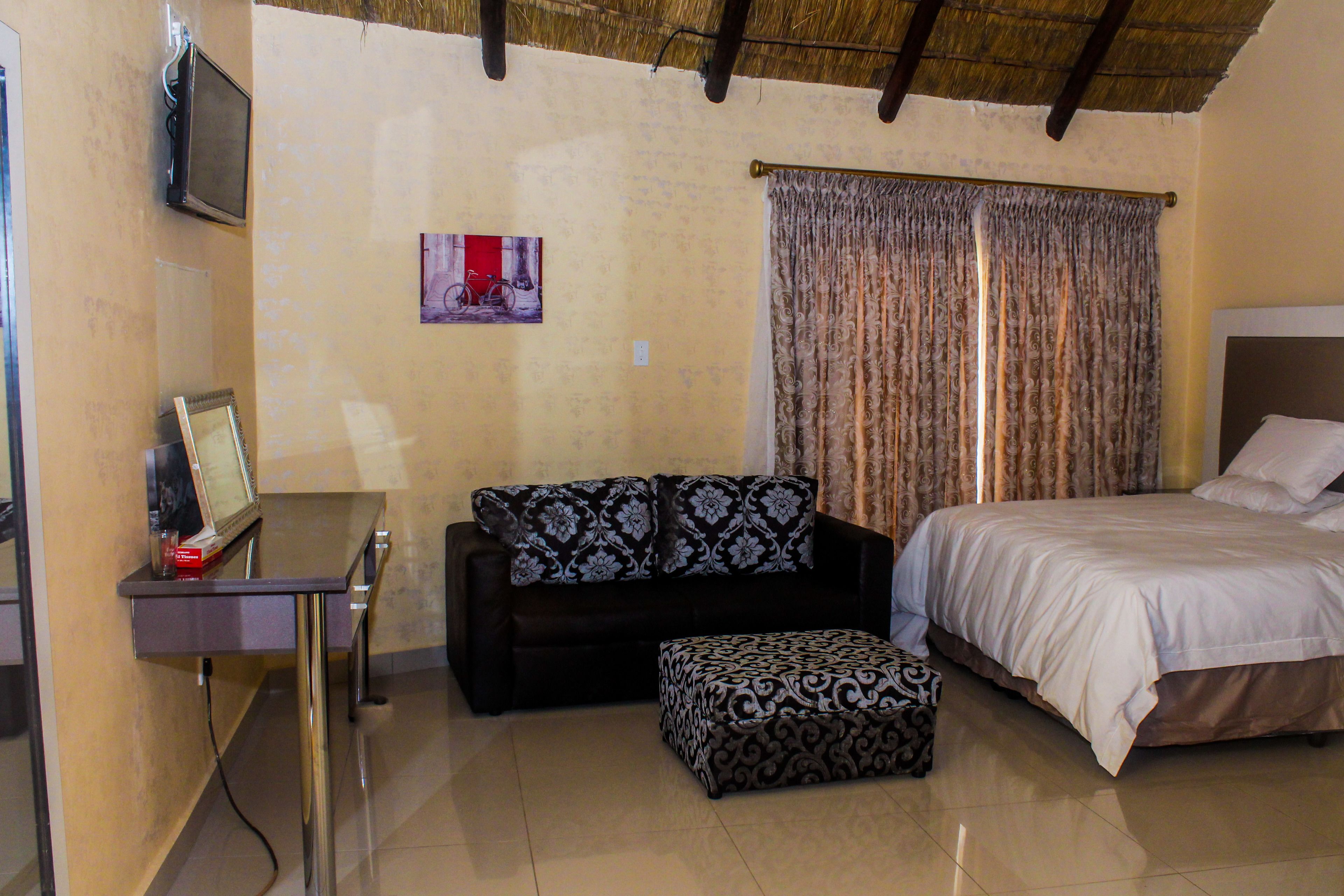 A hotel room with a bed, a sofa, an ottoman, a TV on a desk, and a picture on the wall.