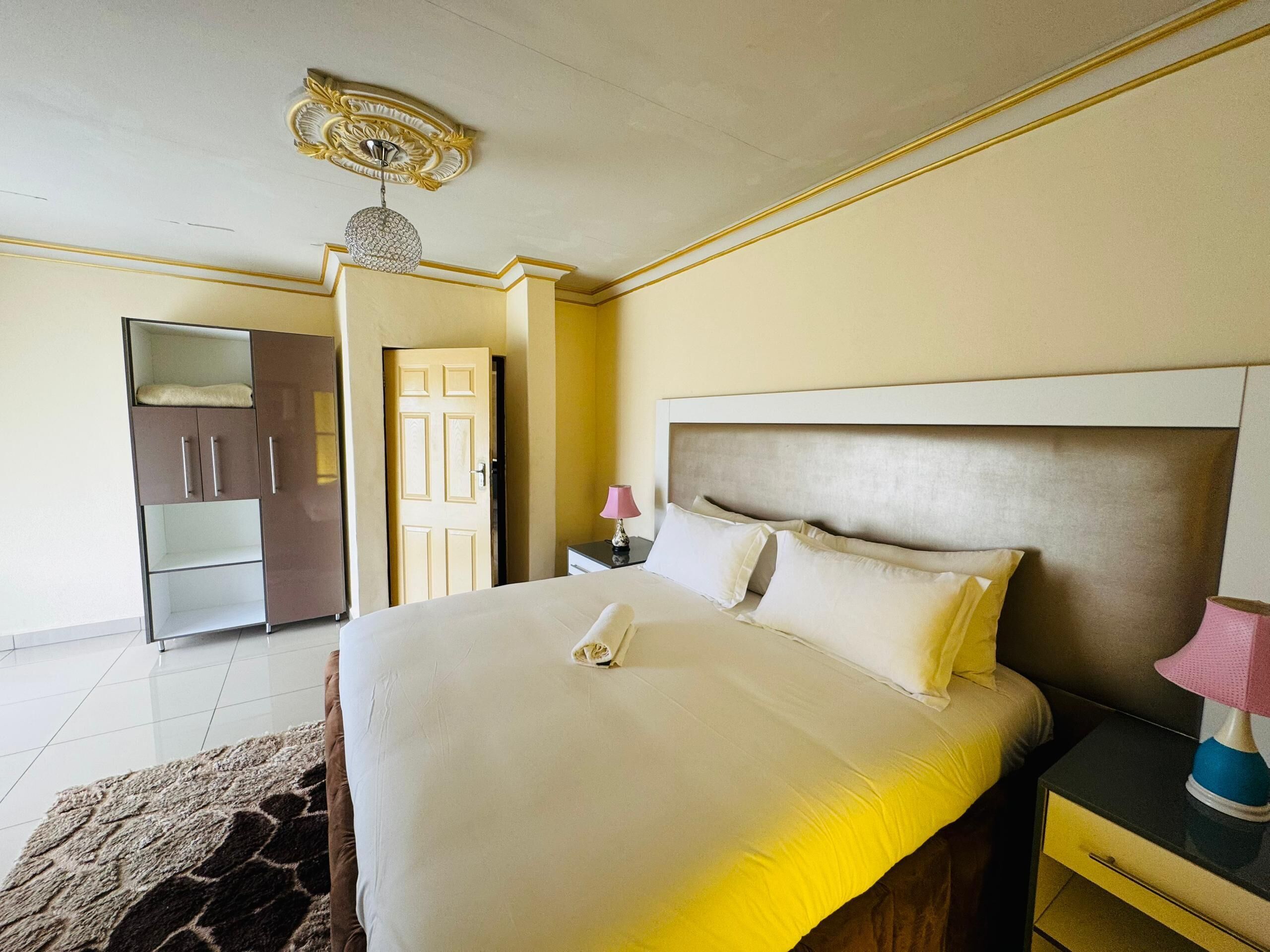 Quarto de hotel com cama, mesa de cabeceira, luminária, guarda-roupa e porta.