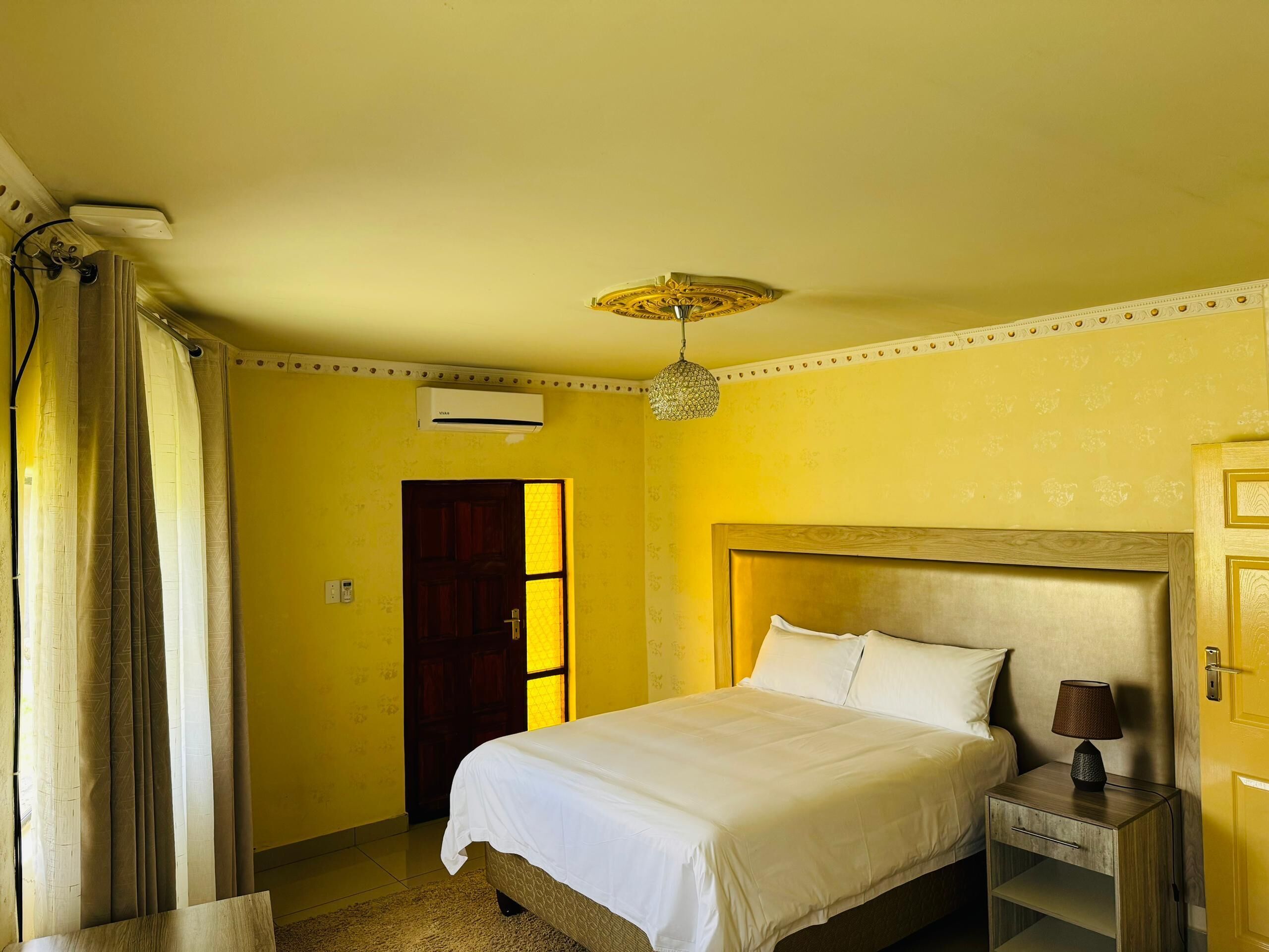 Een hotelkamer met een bed, nachtkastje, lamp, airconditioning en een deur.