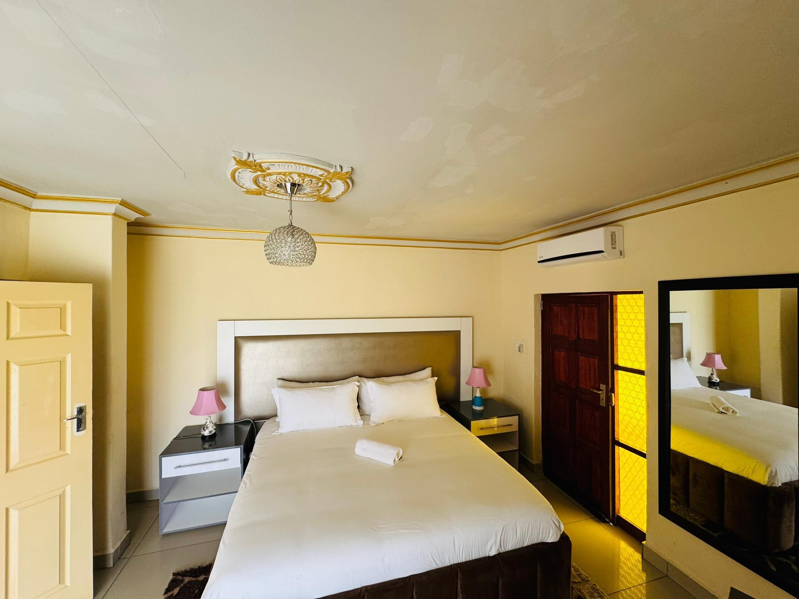 Una habitación de hotel con una cama, mesitas de noche, un espejo y un equipo de aire acondicionado.
