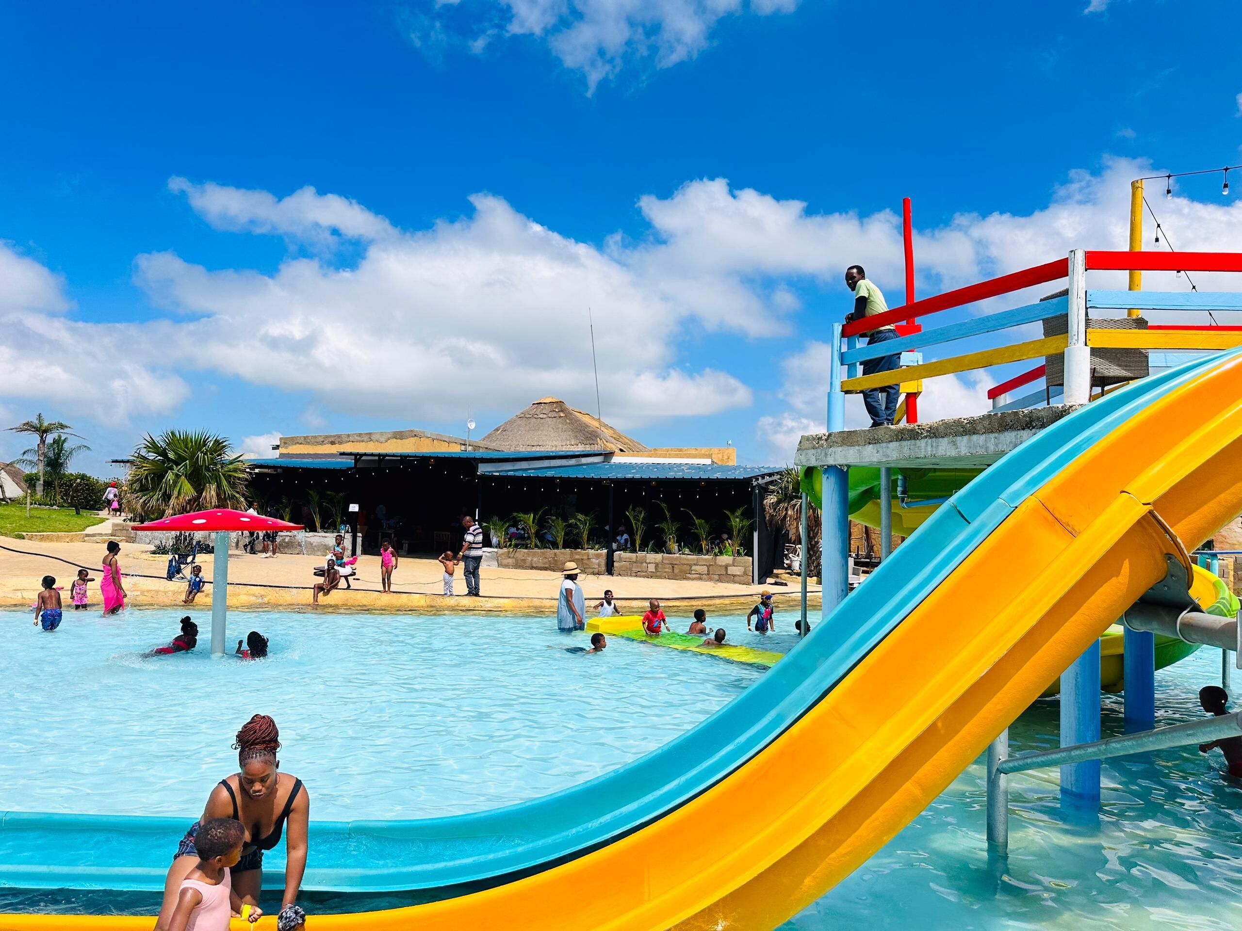 Ein Wasserpark mit großem Pool, einer bunten Rutsche und einem überdachten Bereich mit Sitzgelegenheiten.