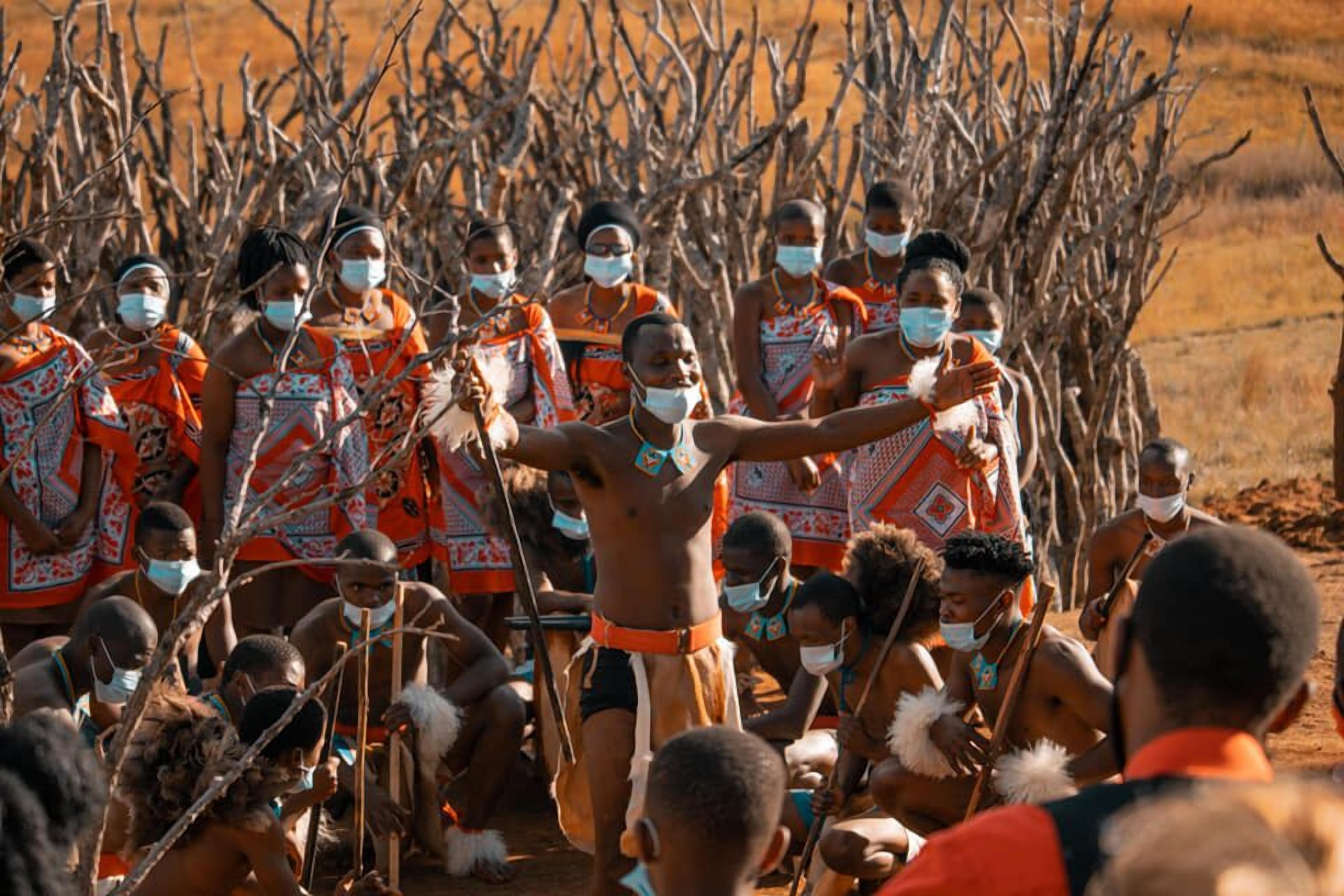 A group of people in traditional attire, some holding objects, gathered outdoors.