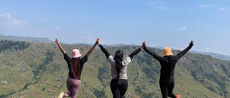 Tres personas en un saliente rocoso, con los brazos levantados, contemplando un paisaje montañoso.