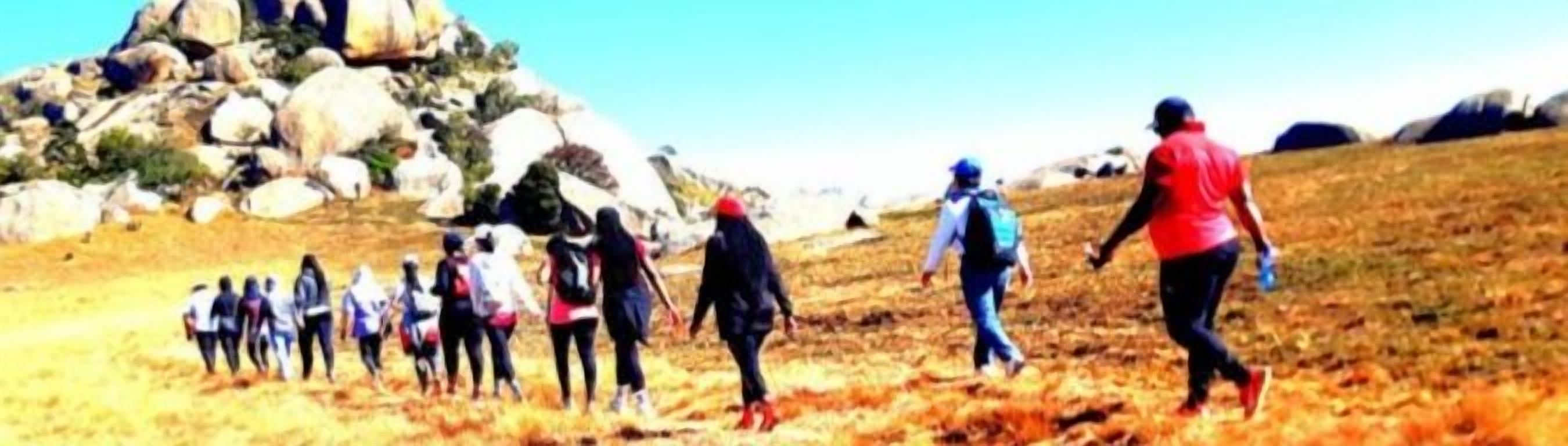 A group of people walking on a grassy hill with rocky formations in the background.