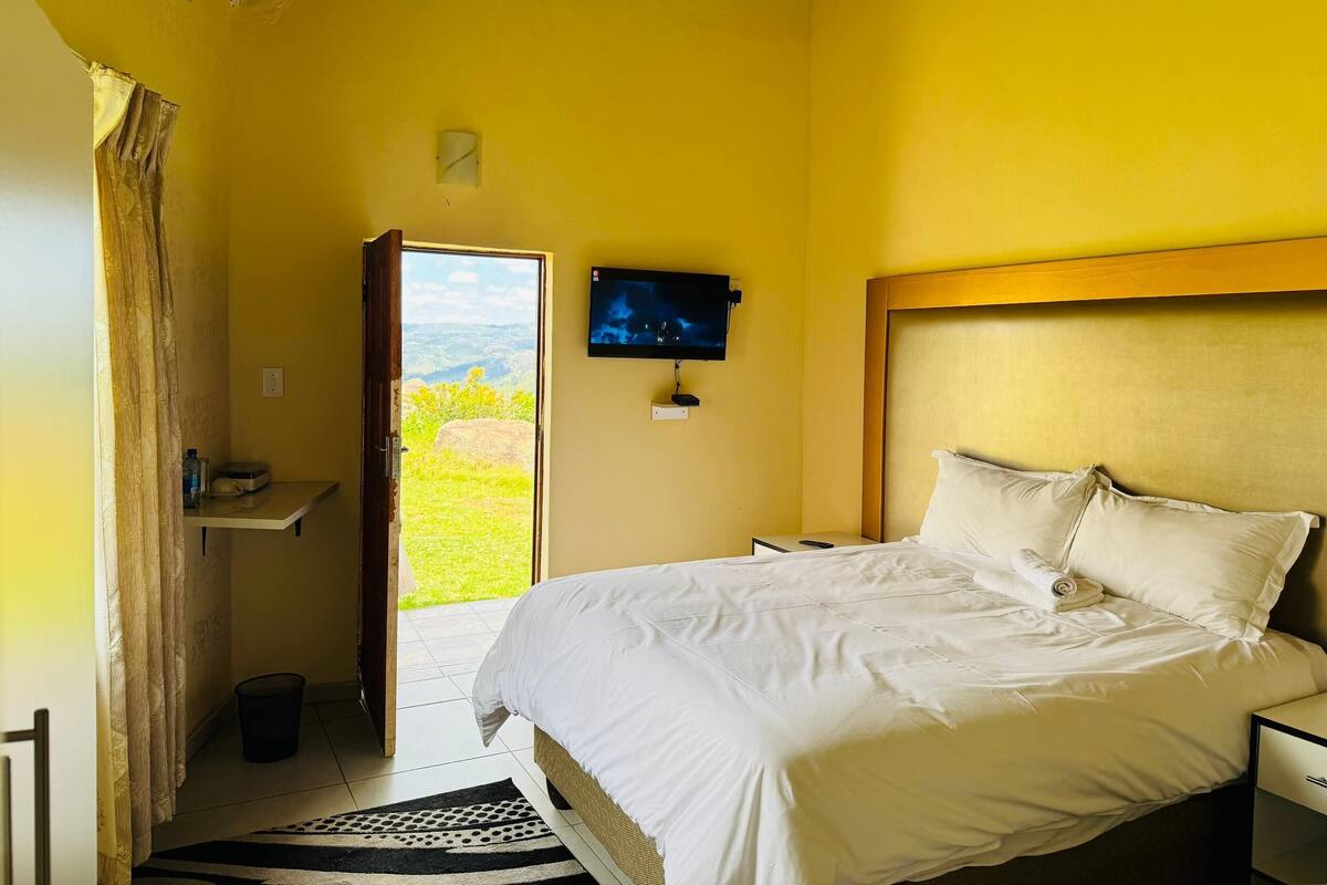A bedroom with a bed, a television, and a view of the outdoors.