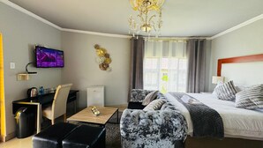 A hotel room with a bed, a sofa, a TV, a desk, and a chandelier.