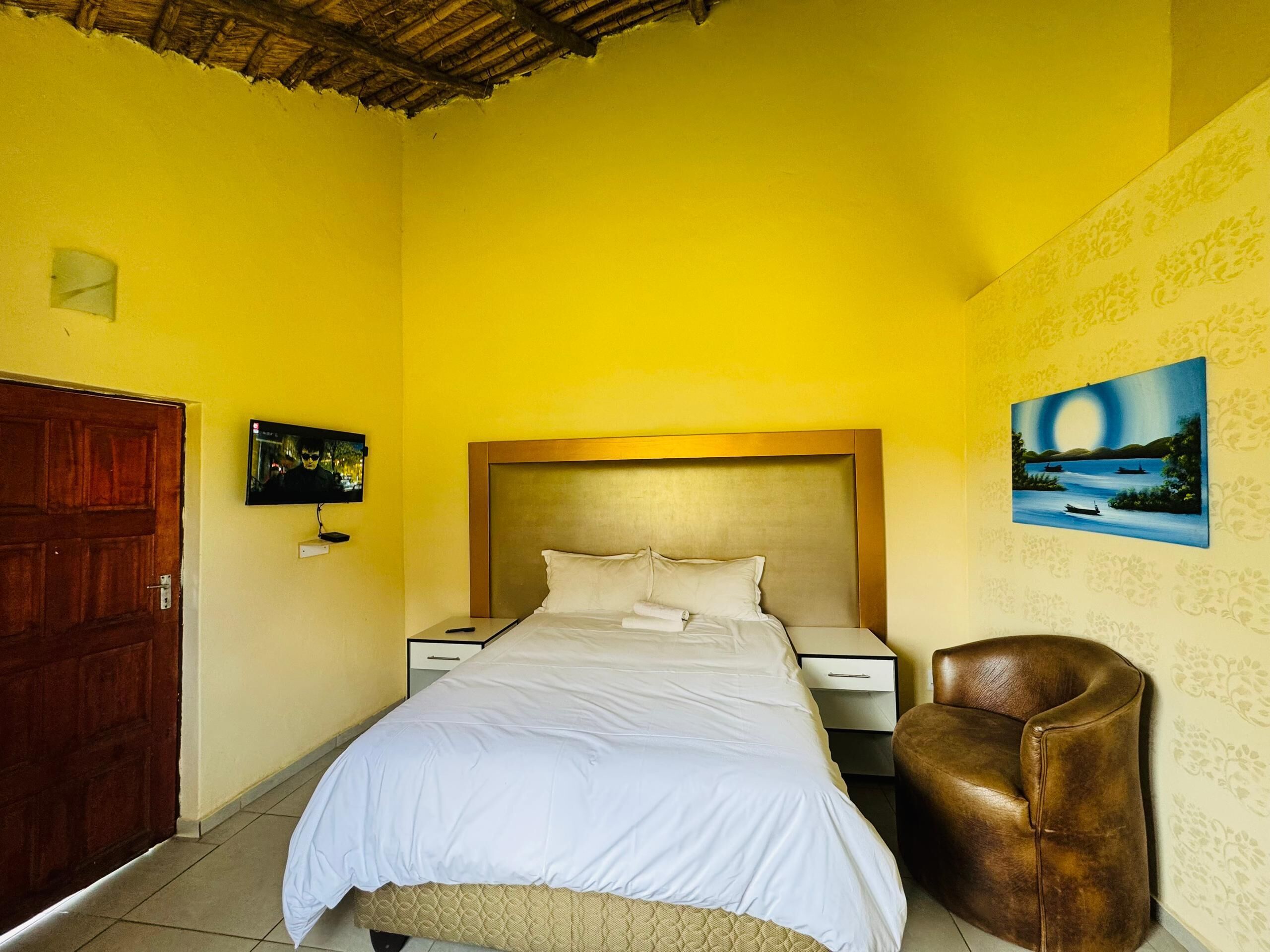A room with a bed, a chair, a wooden door, a nightstand, and a painting on the wall.
