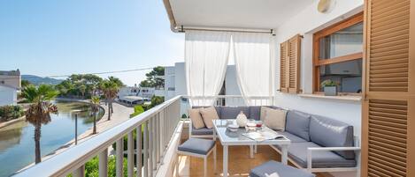 A balcony with a view of a river, a white table with cushions, and a sofa.