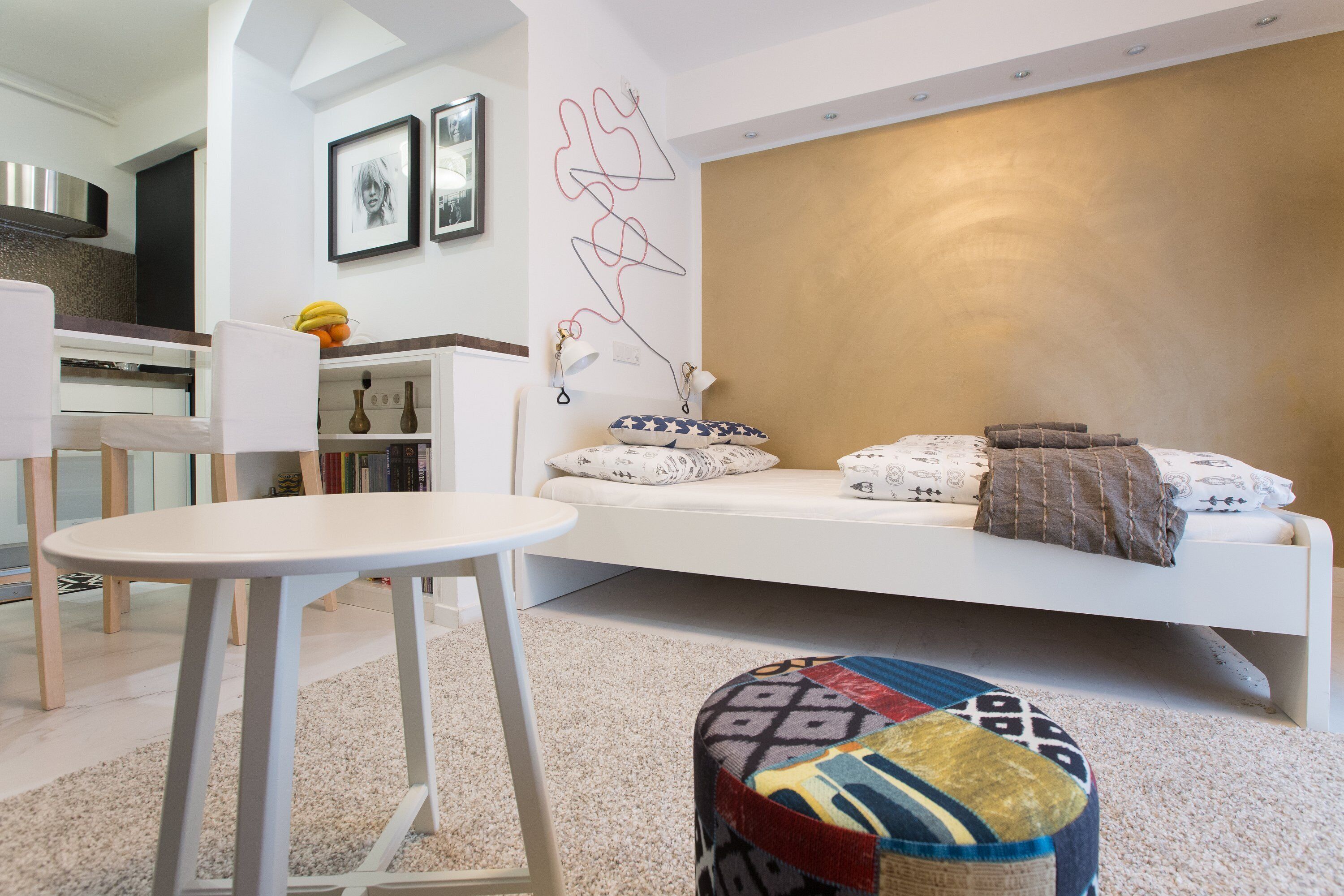 A modern living room with a white sofa, a small round ottoman, and a white table.