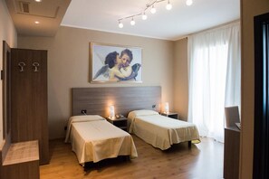 A hotel room with two single beds, a wooden wardrobe, a nightstand with a lamp, and a painting of an angel on the wall. - Albergo Grappolo D'oro (Montebelluna)