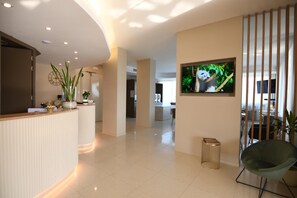 A modern hotel lobby with a reception desk, a large TV screen displaying a panda, and a seating area with a chair. - Albergo Grappolo D'oro (Montebelluna)