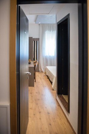 A hotel room with a wooden floor, a bed with a white bedspread, a desk with a chair, and a window with curtains. - Albergo Grappolo D'oro (Montebelluna)