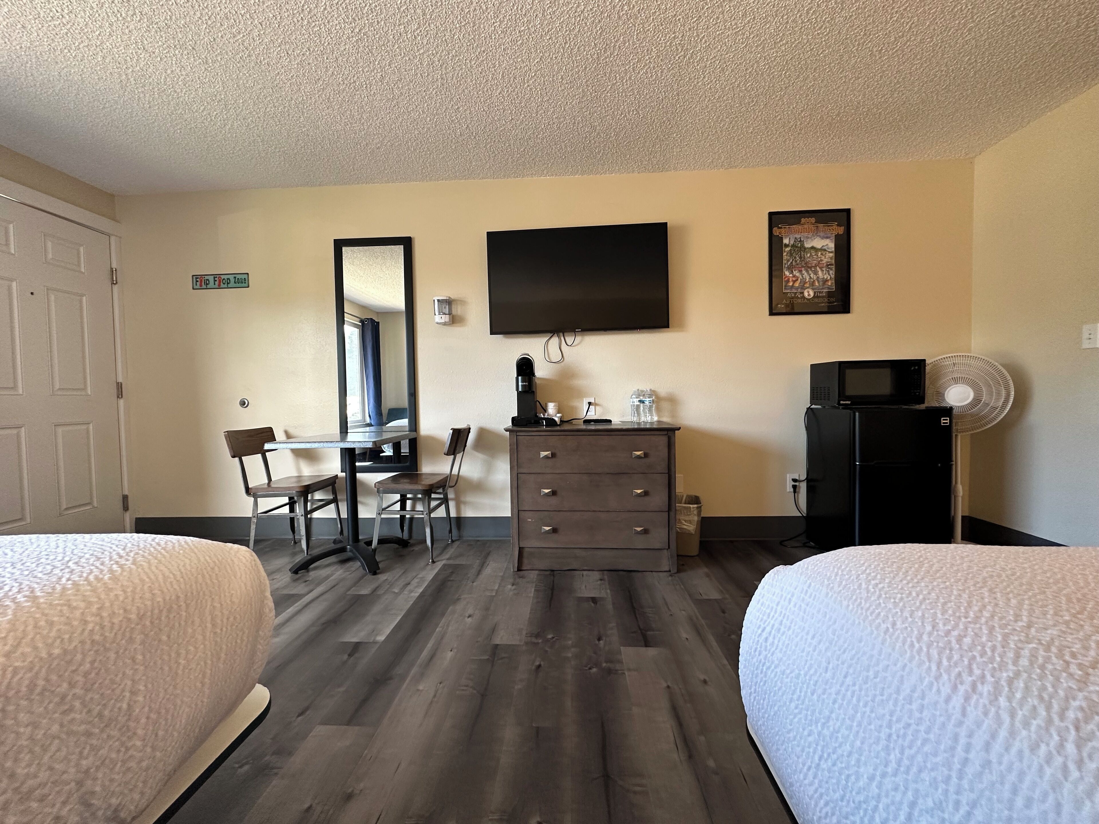 Une chambre d’hôtel avec deux lits, un bureau avec une chaise, une commode, une télévision, un four à micro-ondes et un ventilateur.