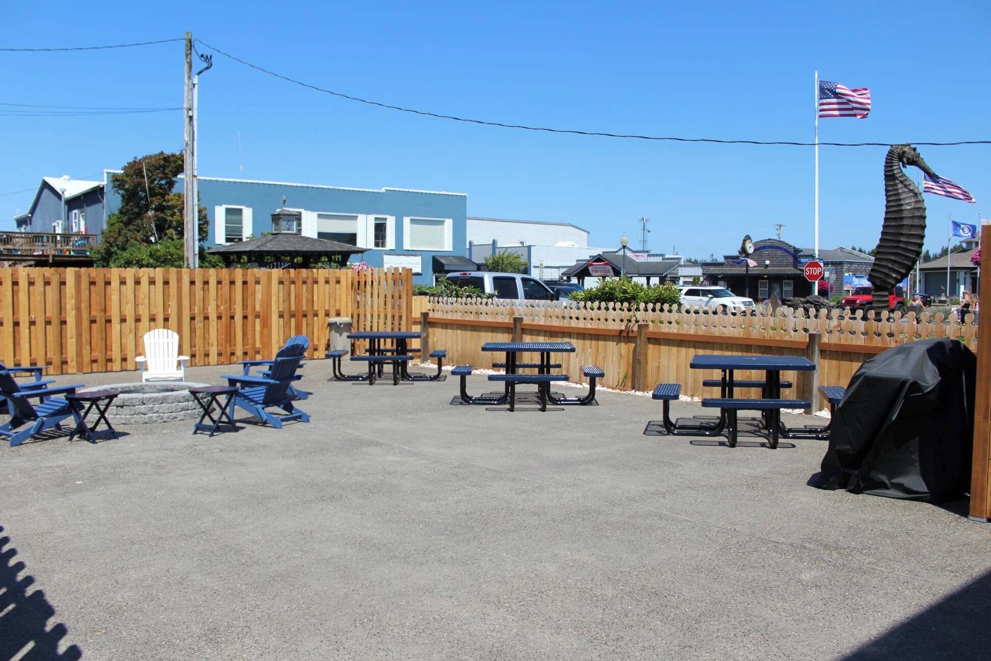 A parking area with picnic tables and chairs, a wooden fence, and a flag.
