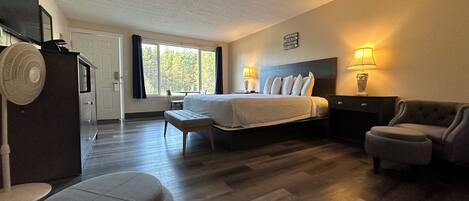 Una habitación de hotel con cama, lámparas de noche, escritorio, silla y ventilador.
