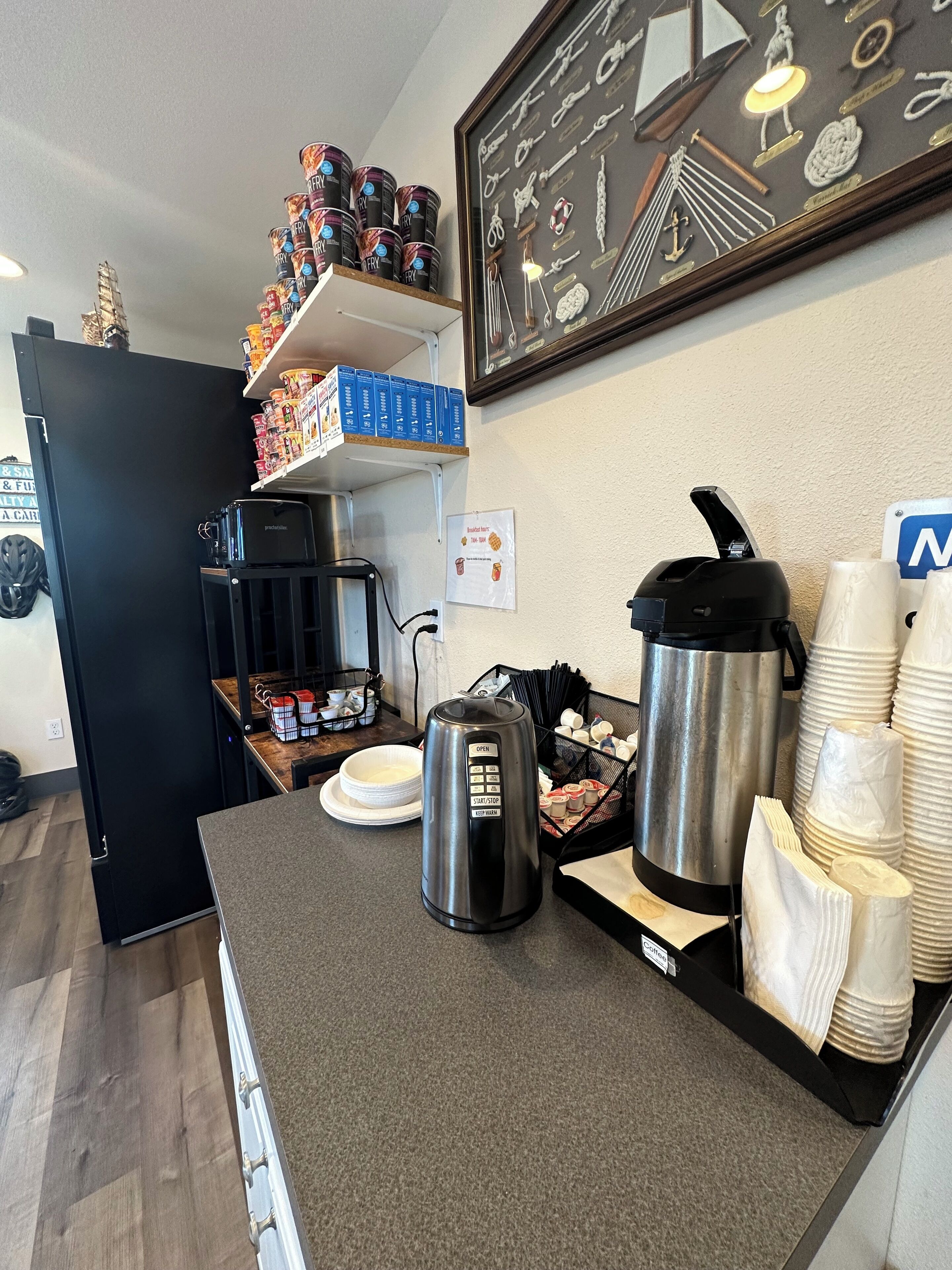 Eine Küchenzeile mit Kaffeemaschine, Wasserkocher und gestapelten Papierbechern.