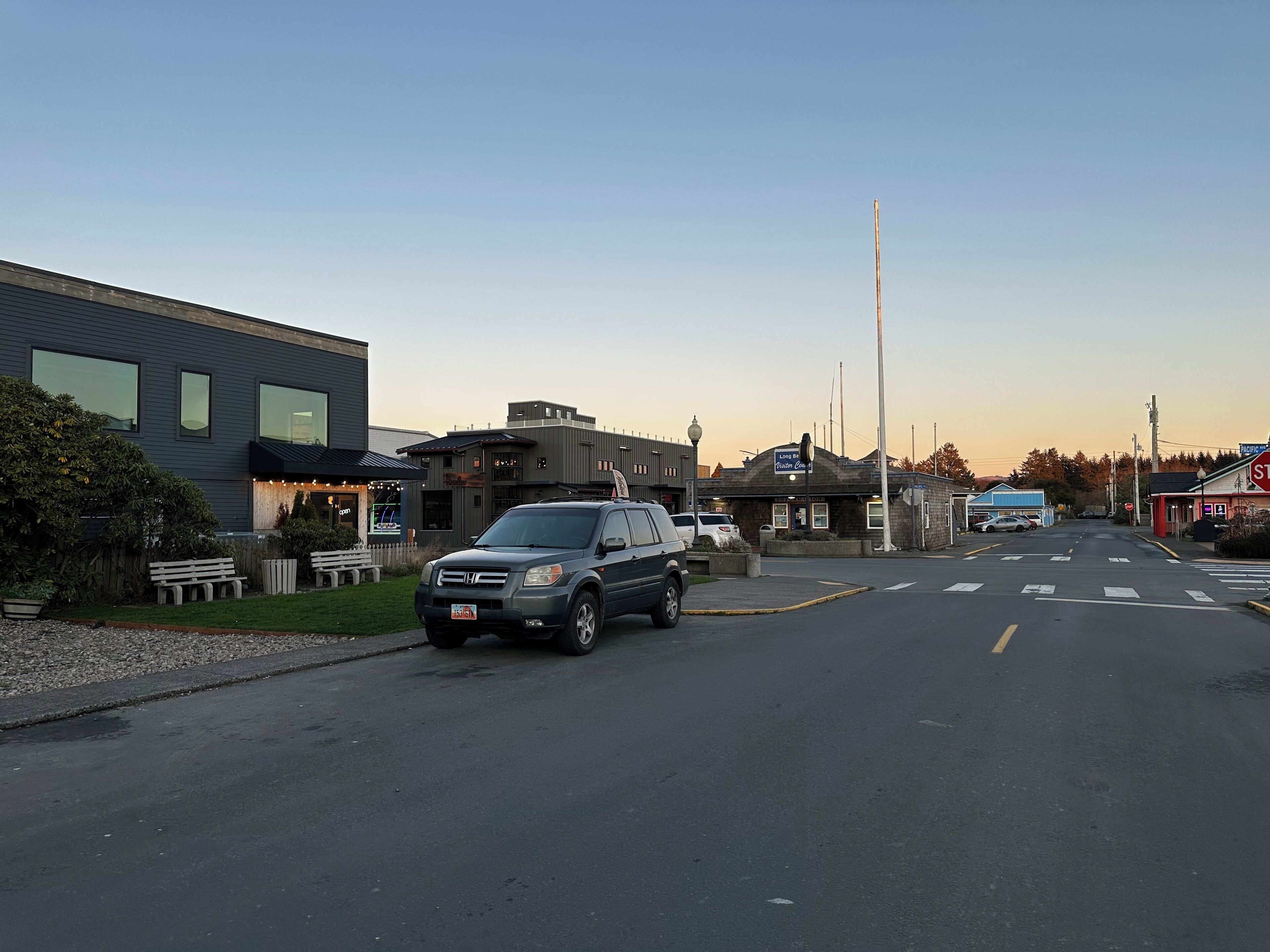 A street view with a modern building, a parked SUV, and a visible storefront with a sign.