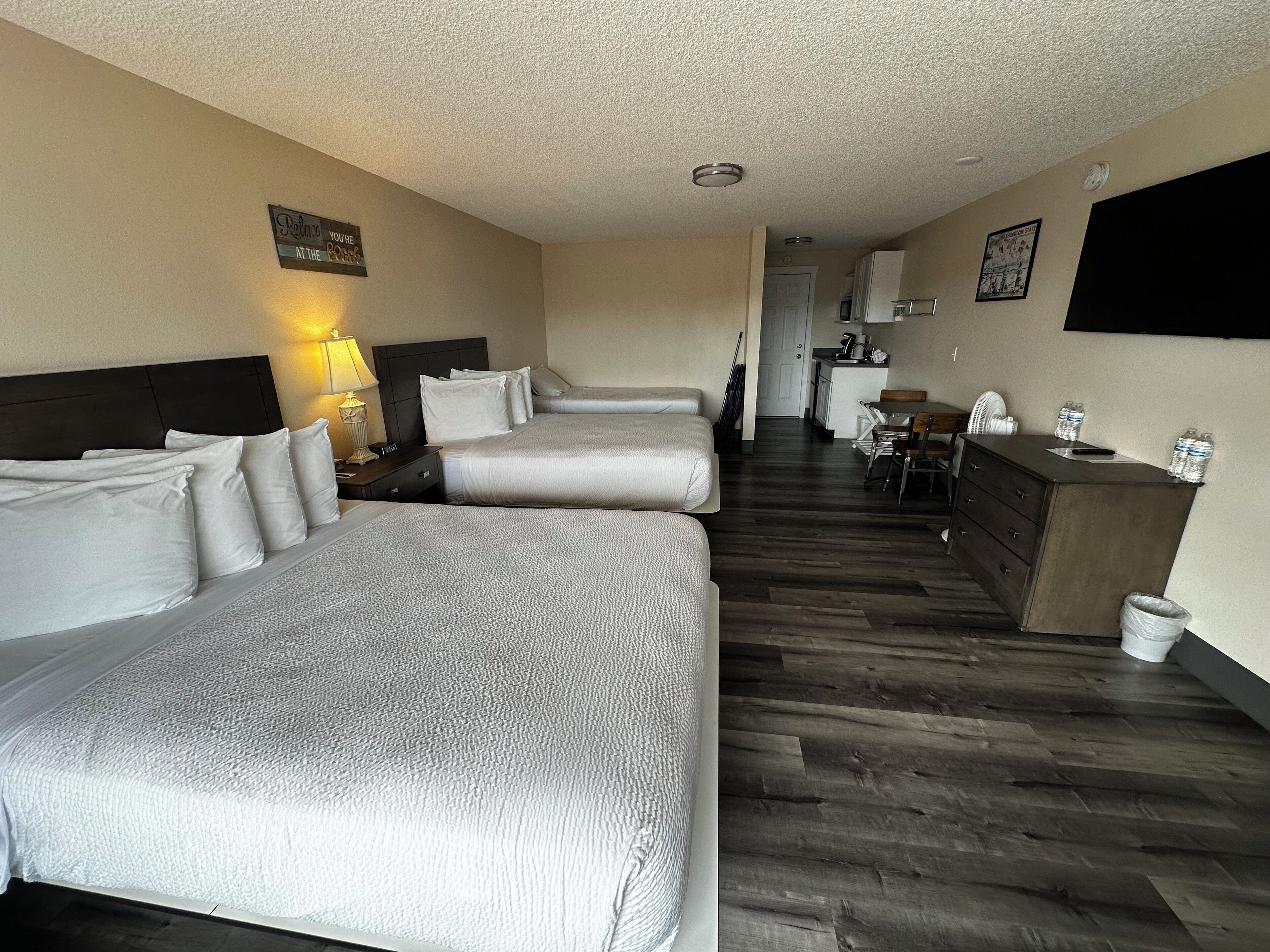 A hotel room with two beds, a small kitchenette, and a dining area.