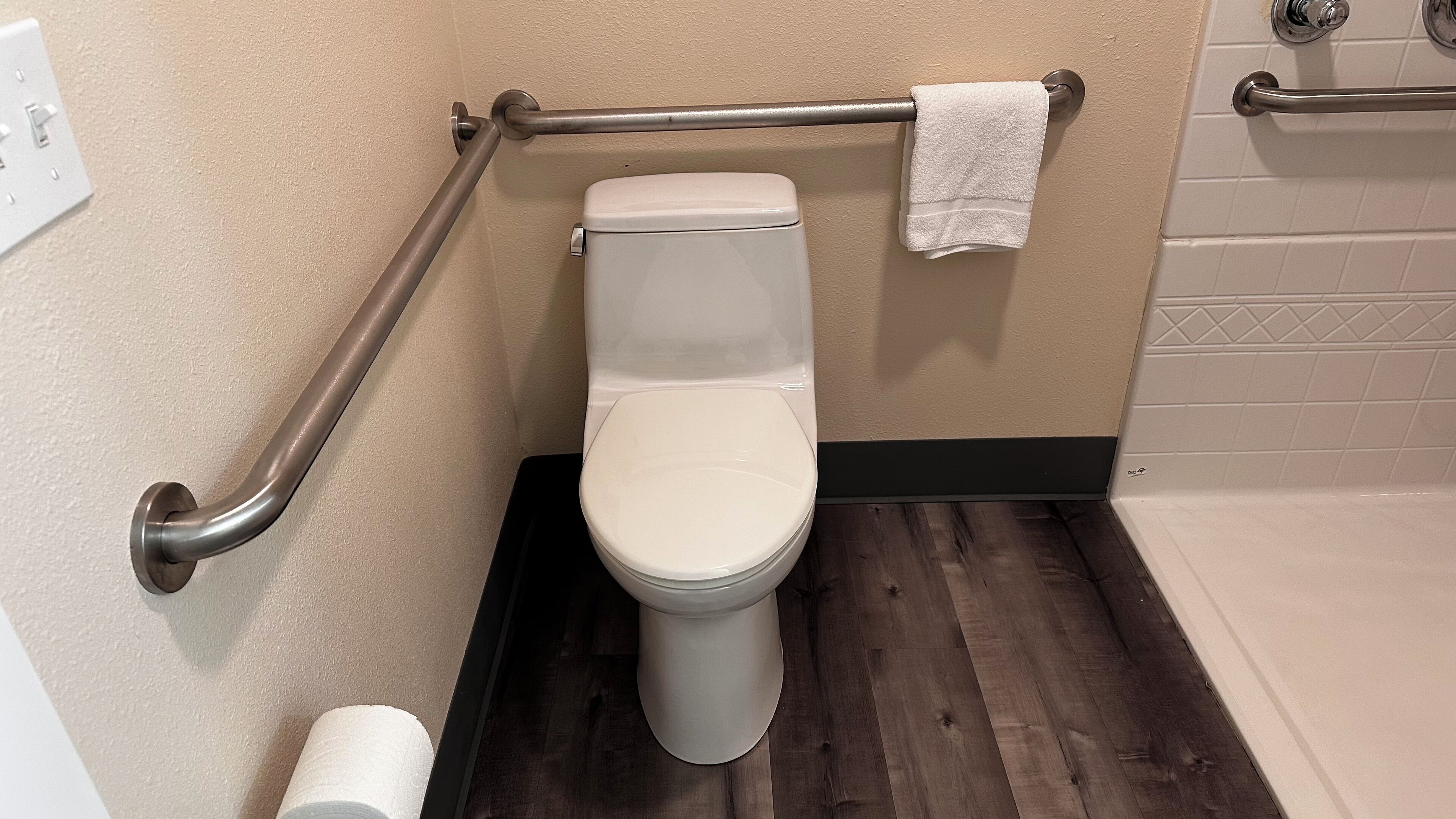 A bathroom with a white toilet, a grab bar, a towel rack, and a toilet paper holder.