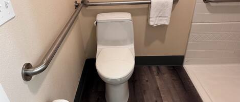 A bathroom with a white toilet, a grab bar, a towel rack, and a toilet paper holder.