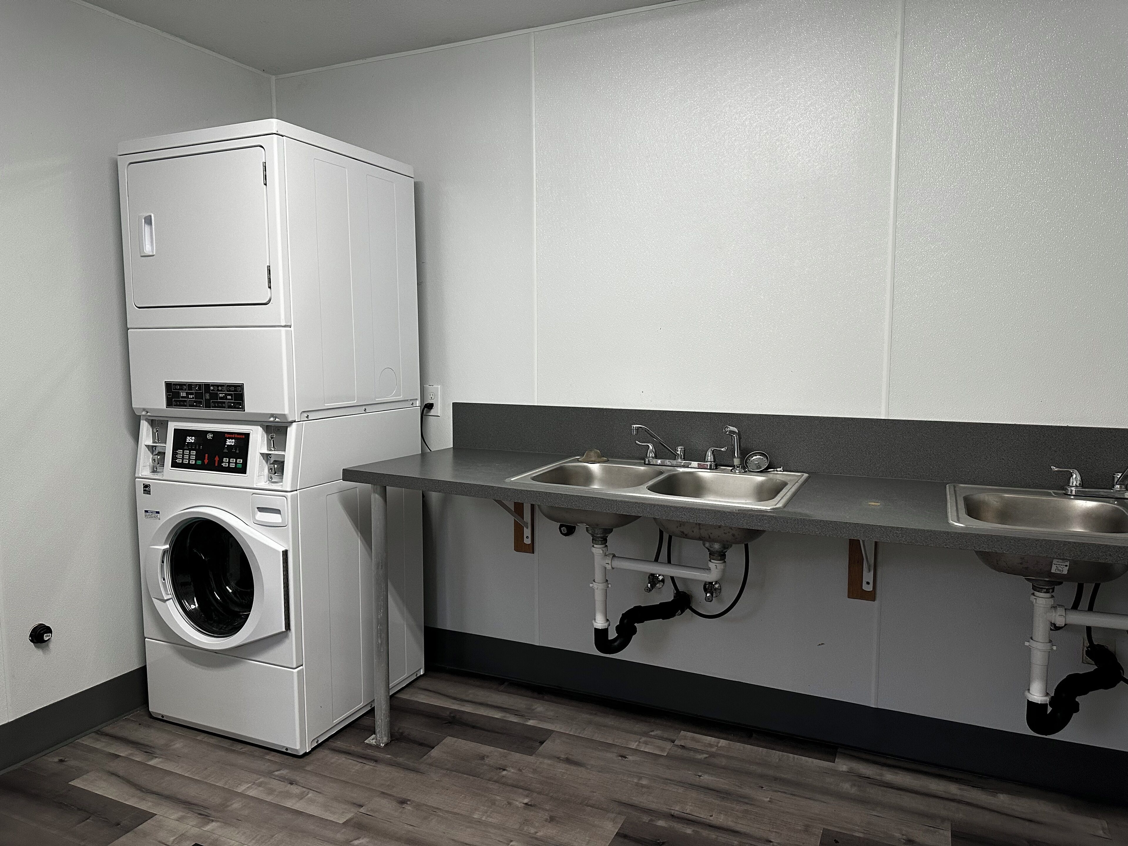 Una cucina compatta con lavatrice e asciugatrice integrate, due lavandini e tubature a vista.