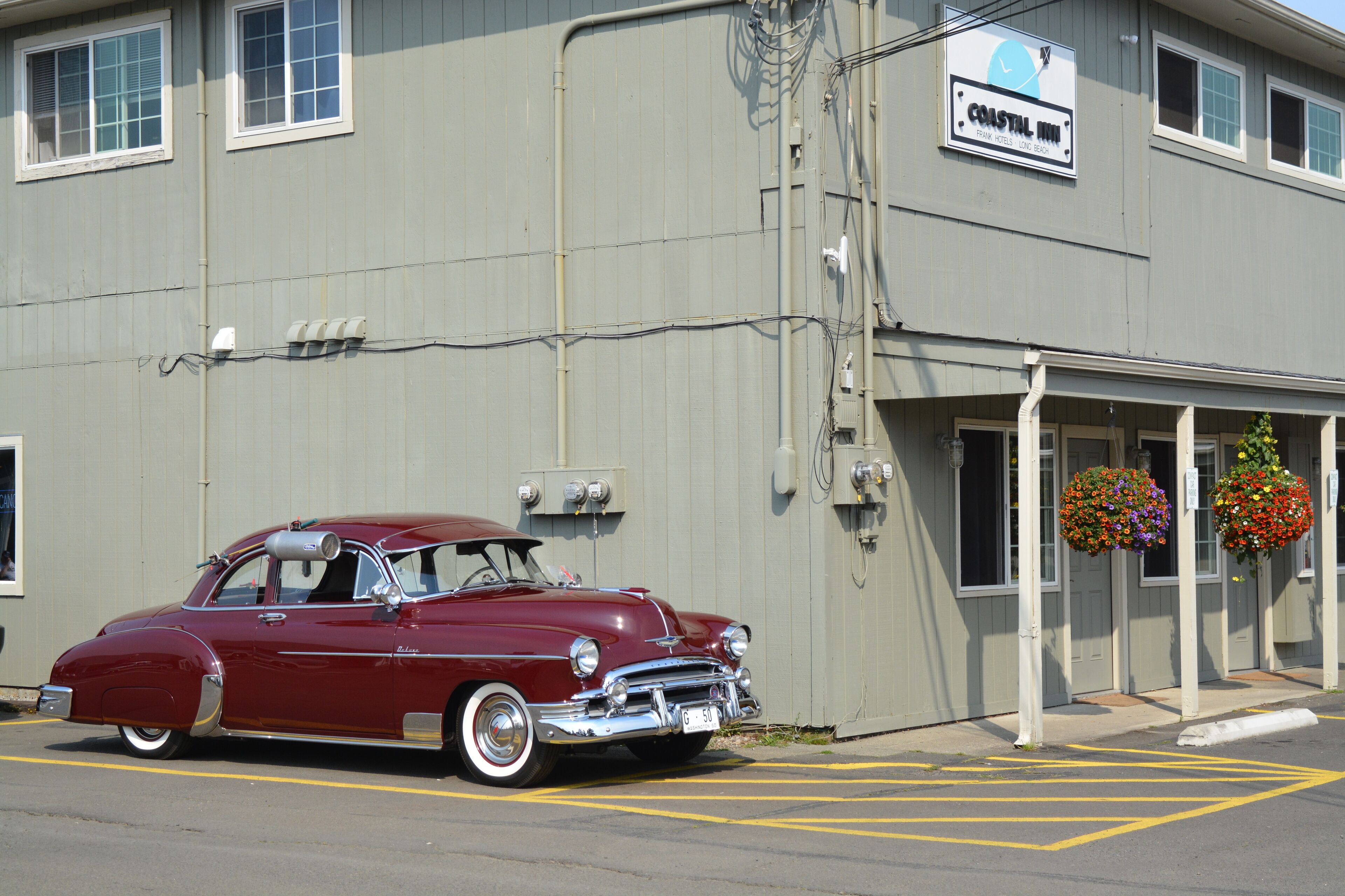 A vintage red car parked in front of a building with a sign reading "Coastal Inn."