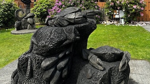 Eine Skulptur eines Seepferdchens in einem Garten, im Hintergrund ein Gebäude.