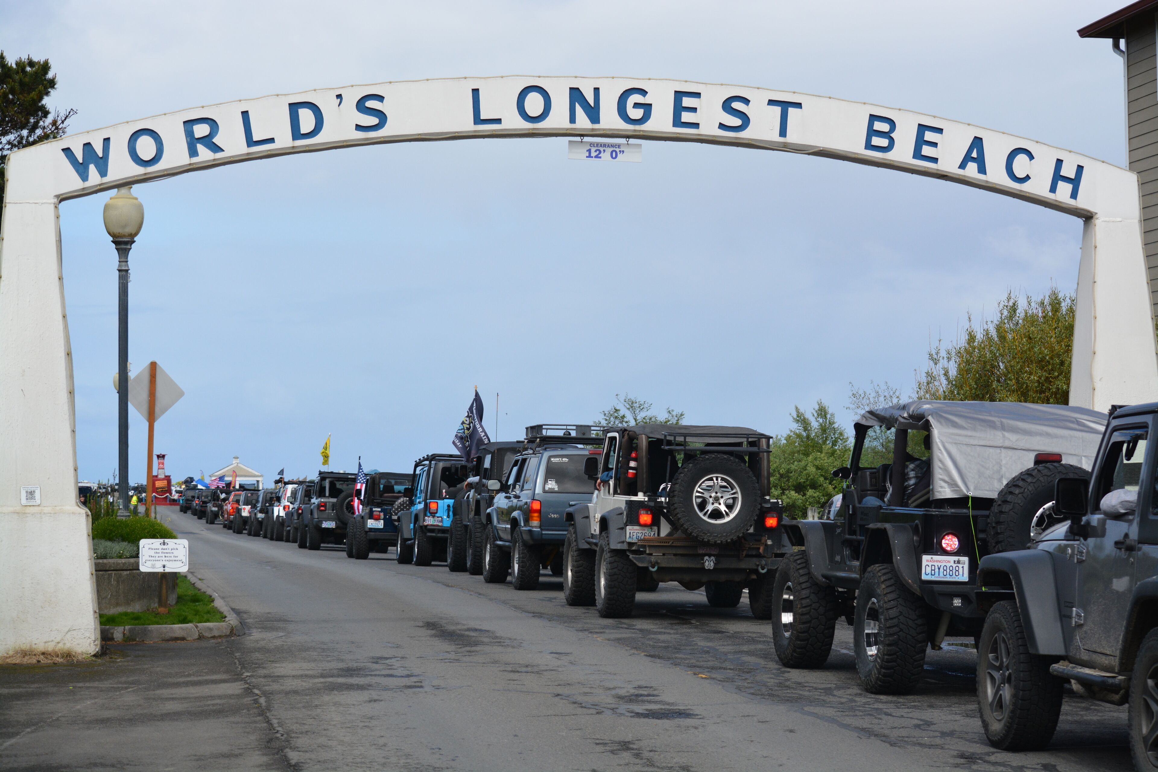 A line of vehicles parked under a sign that reads "WORLD'S LONGEST BEACH".
