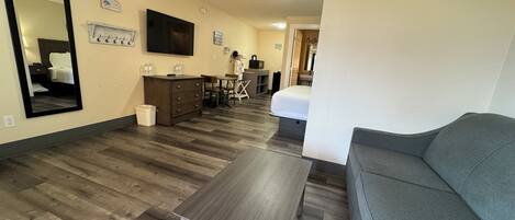 Habitación de hotel con sofá gris, una mesita, televisor, cómoda y espejo.